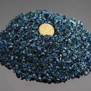 Puede incluir: Un montón de virutas de metal de color turquesa con una moneda de oro encima. Las virutas tienen un brillo metálico y una forma rizada. La moneda es una moneda de 20 céntimos de euro.
