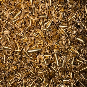 Puede incluir: Una imagen de primer plano de un montón de virutas de metal brillantes de color dorado. Las virutas son de varias formas y tamaños, creando un fondo texturizado y abstracto.
