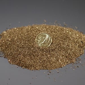 Può includere: Un mucchio di materiale fine, marrone dorato, con una moneta d'oro sopra. La moneta ha il numero 20. Il materiale sembra essere piccole particelle o scaglie, possibilmente utilizzate per l'artigianato o la decorazione.
