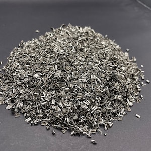 May include: A pile of silver metal scraps, likely from a manufacturing process, on a dark gray surface.