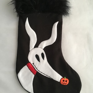 May include: Black Christmas stocking featuring Zero from The Nightmare Before Christmas. The stocking has a black base with a white Zero design, a red collar, and a small orange pumpkin. The top of the stocking is trimmed with black feathers.