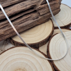 May include: A silver snake chain necklace on a wooden background.