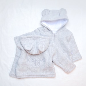 May include: Gray fleece hooded jacket with bear ears, personalized with the name "Reggie" embroidered on the back.