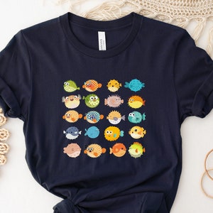 May include: A navy blue t-shirt with a graphic print of colorful pufferfish. The shirt has short sleeves and a crew neck.