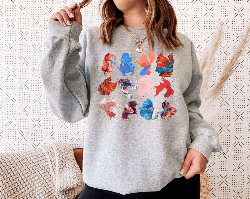 May include: A gray sweatshirt with a colorful print of betta fish. The fish are in various poses and colors, including red, blue, and orange.