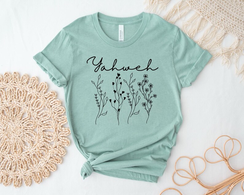 May include: A light green t-shirt with the word "Yahweh" written in black cursive script. The shirt has a floral design with black outlines.