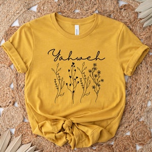 May include: A mustard yellow t-shirt with a black floral design and the word "Yahweh" in cursive.