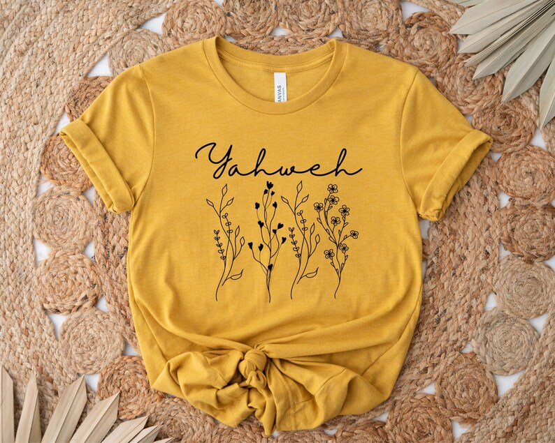 May include: A mustard yellow t-shirt with a black floral design and the word "Yahweh" in cursive.