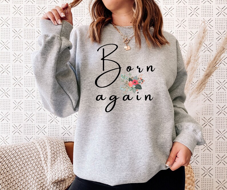 Puede incluir: Sudadera gris con el texto "Born again" en letras cursivas negras y un dise&ntilde;o floral en rosa, rojo y verde.