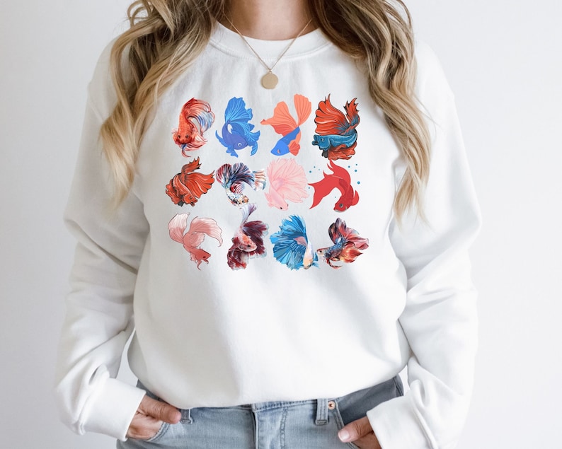 May include: White sweatshirt with a colorful pattern of betta fish. The fish are in various shades of red, blue, pink, and orange.