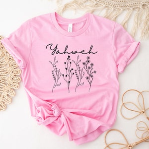May include: A pink t-shirt with the word "Yahweh" and a floral design in black.