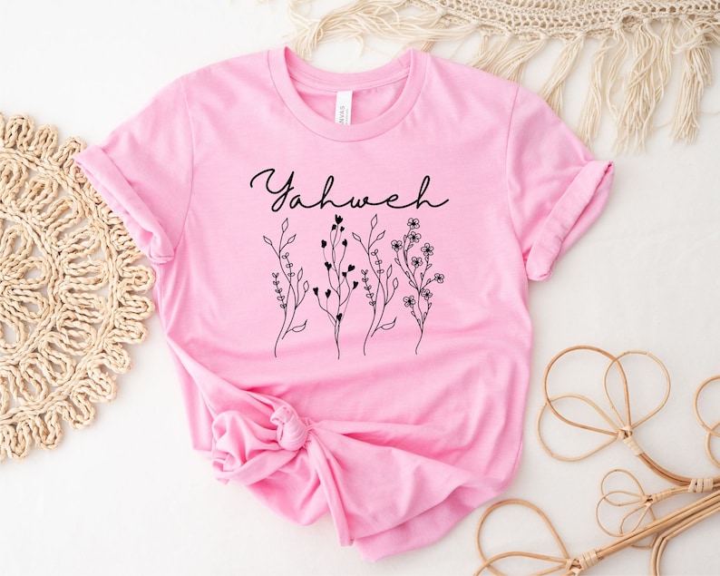 May include: A pink t-shirt with the word "Yahweh" and a floral design in black.