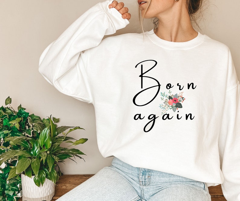 Puede incluir: Sudadera blanca con el texto "Born again" en letra negra con un dise&ntilde;o floral en rosa, rojo y verde.