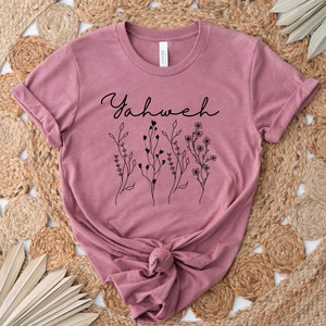 May include: A mauve t-shirt with the word "Yahweh" in black cursive lettering and a floral design.