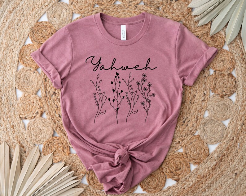 May include: A mauve t-shirt with the word "Yahweh" in black cursive lettering and a floral design.