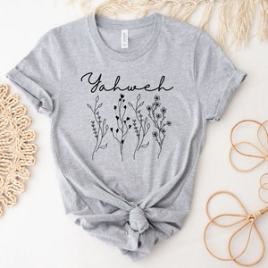 May include: Gray t-shirt with the word "Yahweh" in black cursive lettering and a floral design below it.
