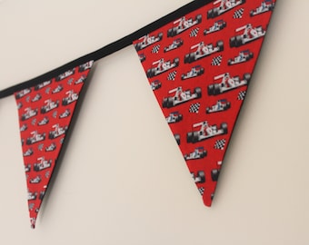 May include: A red and black fabric banner with a repeating pattern of white race cars. The banner is strung up on a wall.