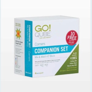 May include: A white box with green and blue accents featuring the text "GO! QUBE Companion Set - Corners". The box includes 4 dies, a cutting mat, a pattern book, and a step-by-step DVD. The box also includes 10 free patterns valued at £18.