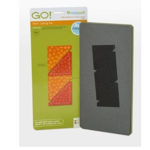 May include: A green and white packaging card with the text "GO! fabric cutting die" and a picture of a die cutting three fabric squares. The die is shown next to the packaging card.