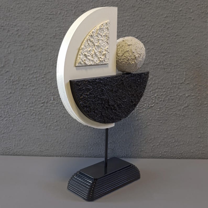 May include: A modern abstract sculpture made of wood and painted in black, white, and gray. The sculpture features a sphere resting on a curved shape, and a base with a layered design.