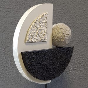 May include: A white, black, and beige abstract sculpture with a textured surface. The sculpture is made of three pieces: a half-circle, a quarter-circle, and a sphere.