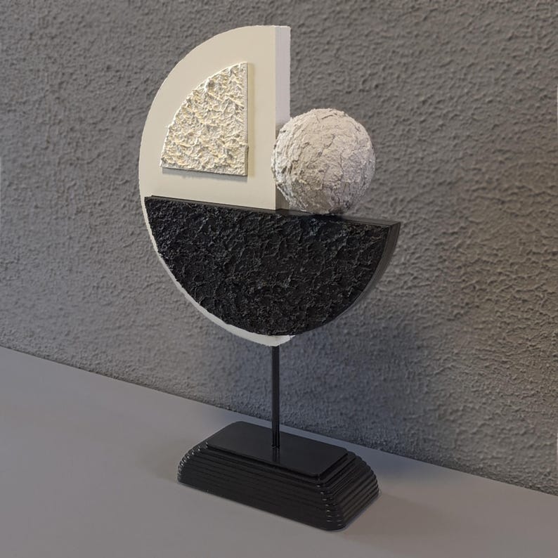 May include: A modern abstract sculpture made of white and black painted wood. The sculpture features a half-circle shape with a smaller white triangle inside. A white sphere sits on top of the half-circle.