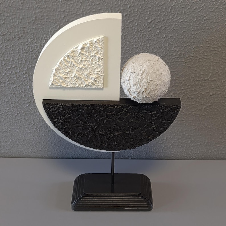 May include: A modern abstract sculpture made of white and black painted wood. The sculpture features a sphere, a half-circle, and a quarter-circle. The sculpture is mounted on a black stand.