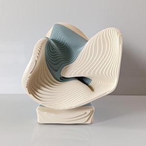 Op de afbeelding: Abstracte sculptuur met een gelaagd ontwerp. De sculptuur heeft een vloeiende vorm met afwisselende lagen van gebroken wit en gedempt blauwgroen. Het staat op een rechthoekige basis, wat een moderne en artistieke uitstraling creëert.