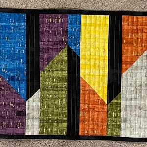 May include: A colorful geometric pattern table runner with alternating stripes of black, white, yellow, orange, blue, green, and purple.
