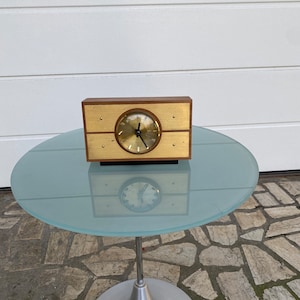 May include: A vintage wooden clock with a gold face and black hands. The clock is sitting on a glass table with a silver base.