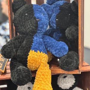 May include: Handmade plush teddy bears in a wooden crate. Each bear is split into two colors: black and blue, with a yellow scarf. The bears are soft and fluffy, perfect for children or as decorative items.