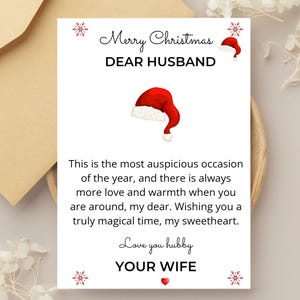 Puede incluir: Una tarjeta de Navidad con una ilustración de gorro de Papá Noel rojo y el texto "Merry Christmas Dear Husband". La tarjeta incluye un mensaje de "Your Wife" deseando un momento mágico.
