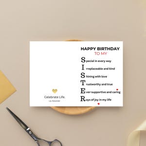 May include: A white greeting card with the text "HAPPY BIRTHDAY TO MY SISTER" in black and red. The card includes an acrostic poem describing a sister. A gold heart and the words "Celebrate Life. Liju Alexander" are also present.