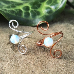 May include: Two wire rings with a white opal stone. The ring on the left is silver and the ring on the right is copper.
