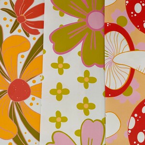 May include: Three different patterned fabric swatches. The first swatch features a yellow and orange flower with green leaves on a white background. The second swatch features a pink and green flower on a white background. The third swatch features a red and white mushroom on a peach background.