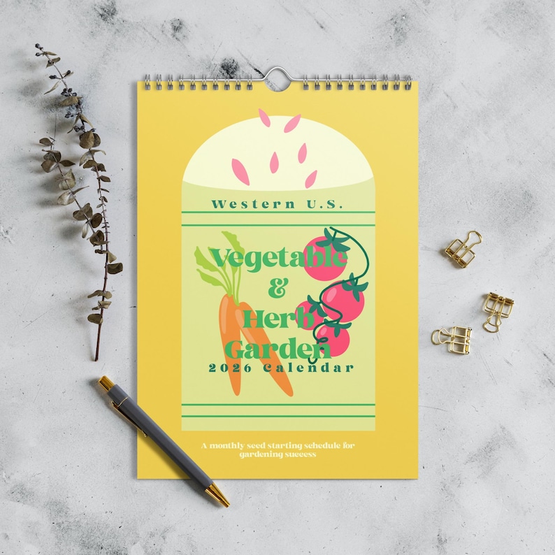 May include: A yellow 2026 calendar with a spiral binding, featuring a design of vegetables and herbs. The calendar includes the text "Western U.S." and "Vegetables & Herbs Garden". A pen and paper clips are also visible.