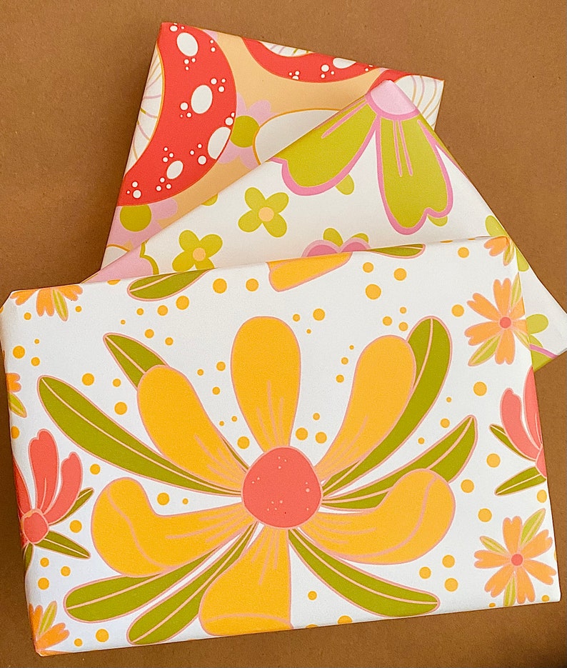 May include: Three sheets of wrapping paper with different floral patterns. The top sheet features a red and white mushroom design, the middle sheet has pink and green flowers, and the bottom sheet has a large yellow flower with green leaves.