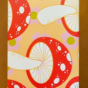 May include: A sheet of wrapping paper with a repeating pattern of red and white mushrooms on a light orange background. The mushrooms have white spots and a white stem.