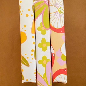 May include: Three wrapped canvases with different retro floral patterns. The canvases are white with pink, yellow, green, and orange flowers and swirls.