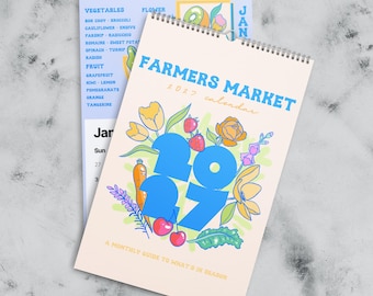May include: A 2027 Farmers Market wall calendar with a spiral binding. The cover features large blue numbers 2027 surrounded by colourful illustrations of flowers, strawberries, cherries, and a carrot on a cream background with text.