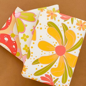 May include: Three sheets of wrapping paper with a retro floral design. The paper features large yellow flowers with pink centers and green leaves on a white background. One sheet has a mushroom design with red and orange mushrooms on a yellow background. The other sheet has a pink and green floral design on a white background.