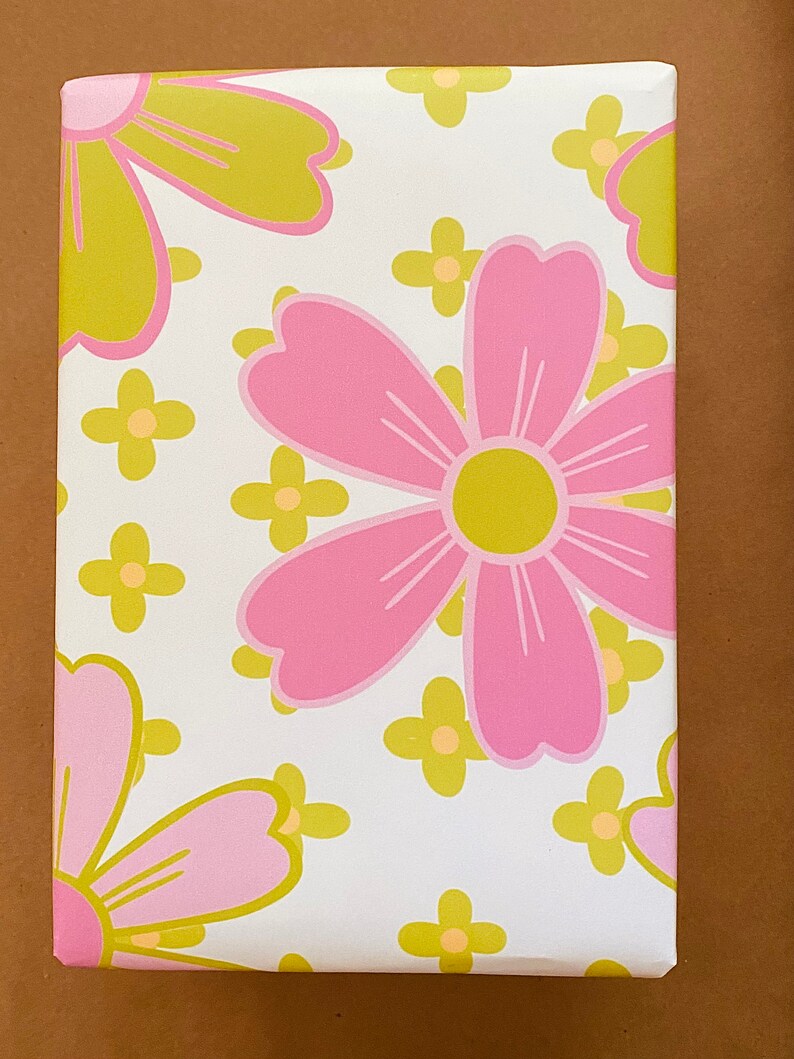 May include: White wrapping paper with a pink and yellow floral pattern. The flowers are stylized and have a retro look.