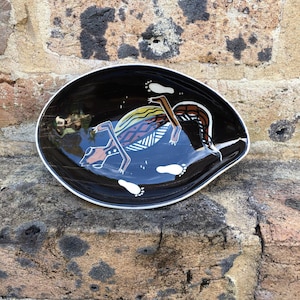 May include: A black ceramic dish with a white and brown design of an animal with footprints. The dish is oval shaped and has a glossy finish.