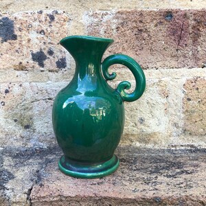 May include: A green ceramic jug with a decorative handle. The jug has a glossy finish and a rounded body.