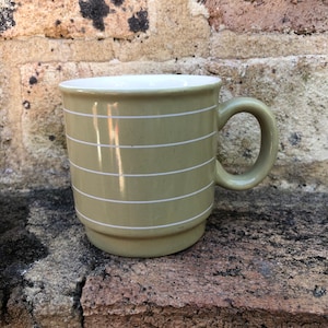 May include: A green ceramic mug with white stripes. The mug has a rounded handle.