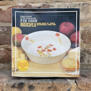 May include: A vintage Field Poppy oven cookware pie dish in its original box. The white dish features orange floral designs and a ribbed exterior. The box includes text: "Refrigerator to oven-oven to table, regular oven or microwave oven use, dishwasher safe." The dish is 22.86 cm in diameter.