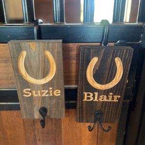 May include: Two wooden signs with horseshoes and hooks. The signs are brown and have the names "Suzie" and "Blair" engraved on them.