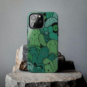 Peut inclure: Une coque de t&eacute;l&eacute;phone verte avec un motif de cactus et de succulentes en dessin anim&eacute;. La coque a une d&eacute;coupe pour l'appareil photo et une bordure noire.