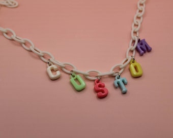 Puede incluir: Un collar de cadena de plástico blanco con abalorios de letras de plástico de colores que deletrean "CUSTOM".