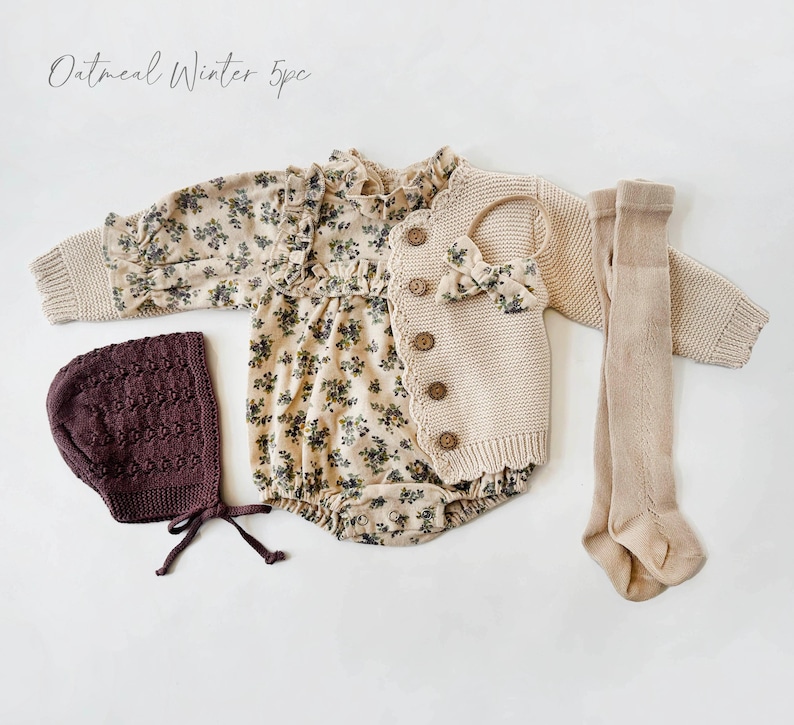 May include: A five-piece baby outfit set in oatmeal color. The set includes a floral print romper, a knitted cardigan, a knitted hat, and a pair of tights. The outfit is perfect for winter.